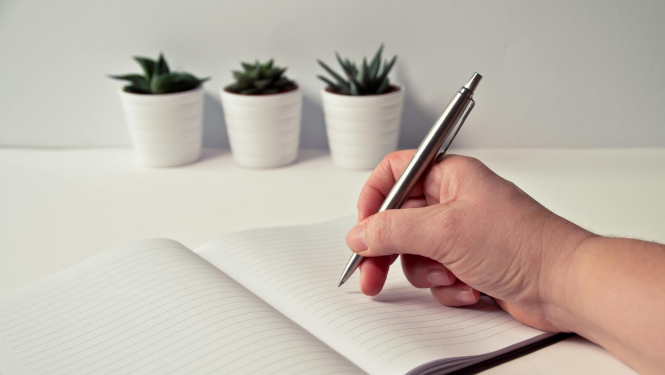 Roka, klade, pildspalva, trīs puķu podi uz galda