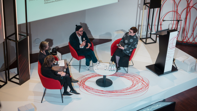 Četri cilvēki sēž modernā konferenču telpā apaļajā diskusijā