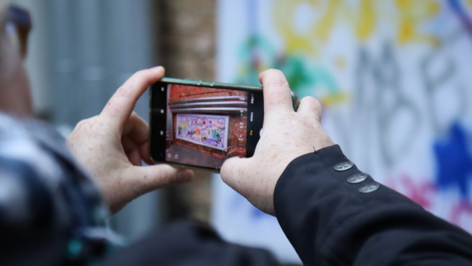 Rokas ar telefonā atvērtu kameras aplikāciju