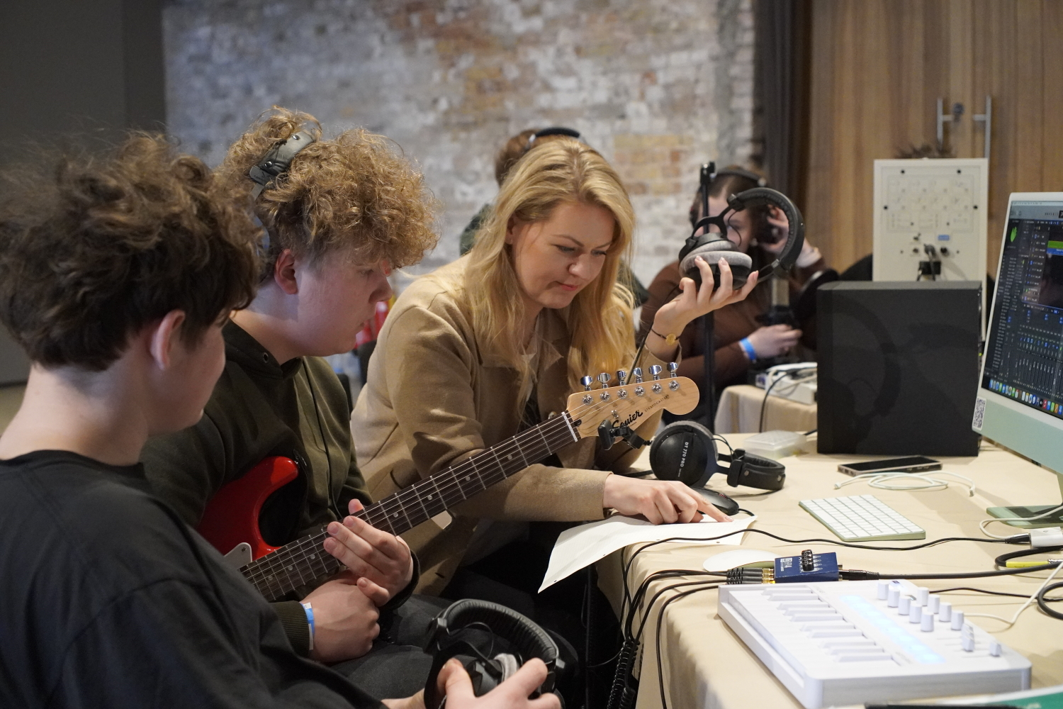 Trīs cilvēki pie galda ar skaņu tehniku, mūzikas instrumetniem