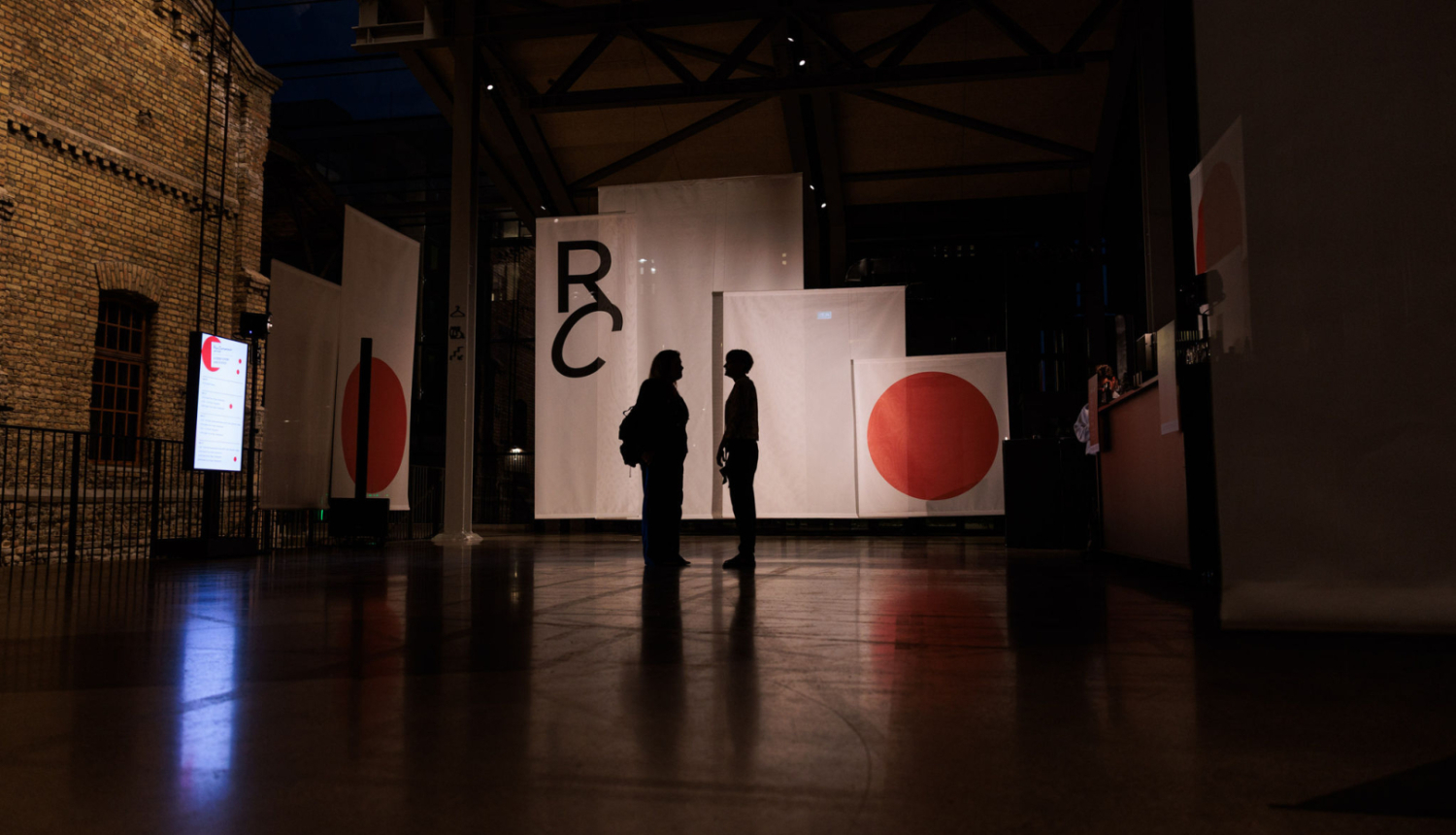 Riga Contemporary atklāšanas vakarā izstāde Hanzas peronā, uz baneru fona divu cilvēku figūras. Foto: Ģirts Raģelis