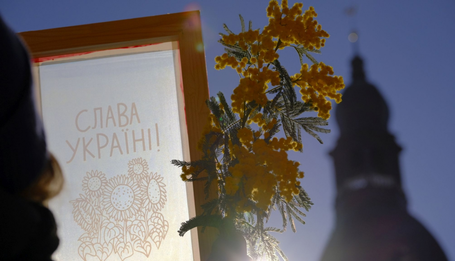 Sietspiedes tehnikā darināts ornaments un dzelteni ziedi uz debesu fona