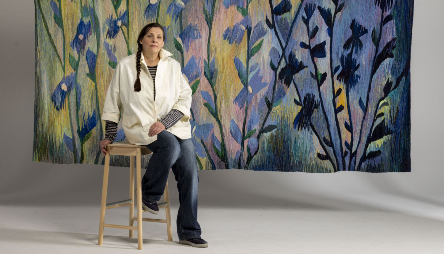 Tekstilmākslinieces Ivetas Vecenānes portrets ar gobelēnu “Cigoriņi” (2019). 2025. Foto: Didzis Grodzs