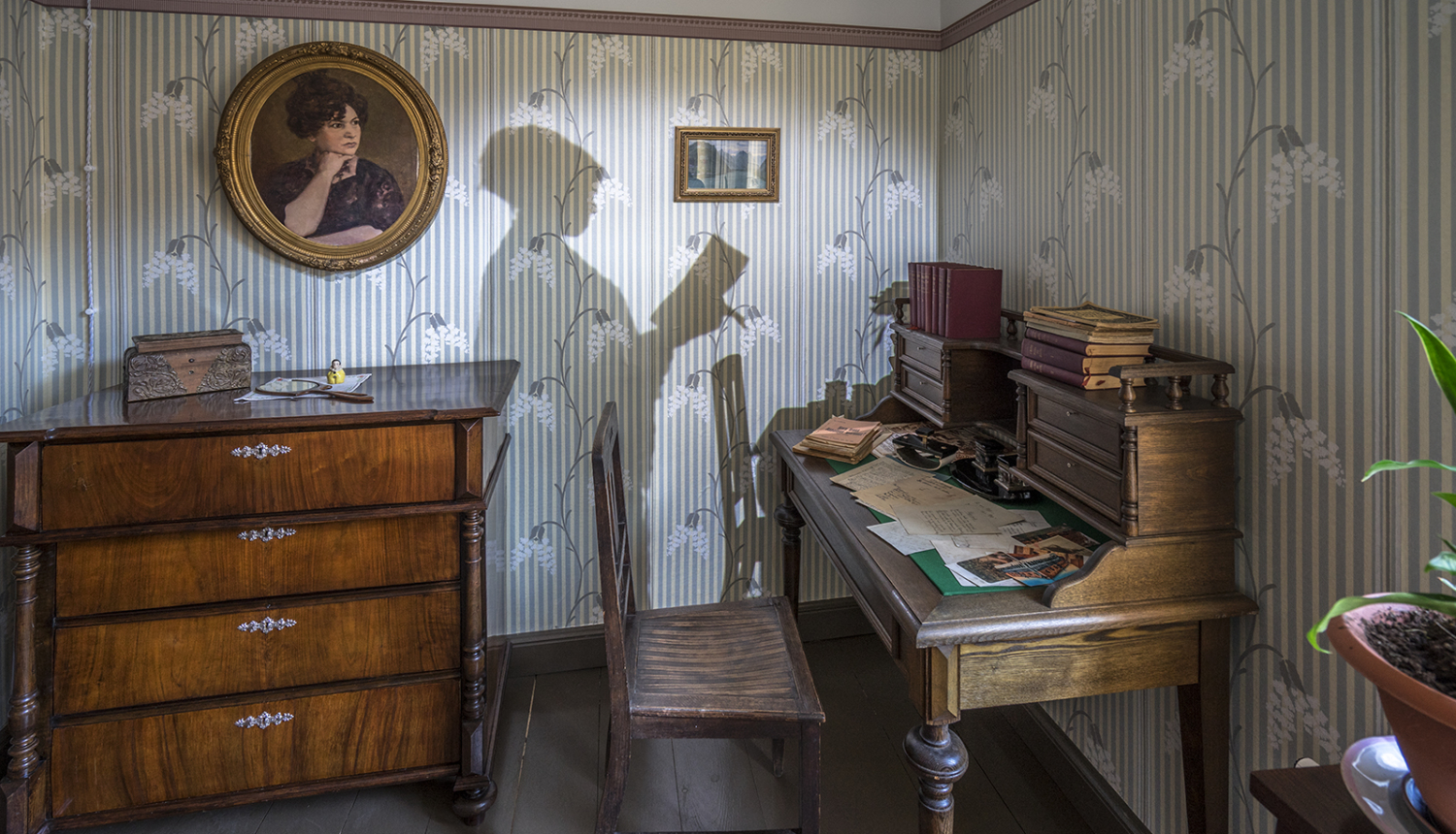 Ekspozīcija Raiņa un Aspazijas mājā Rīgā - istaba, rakstāmgalds, kumode un Aspazijas ēnas siluets, kas projecēts uz sienas