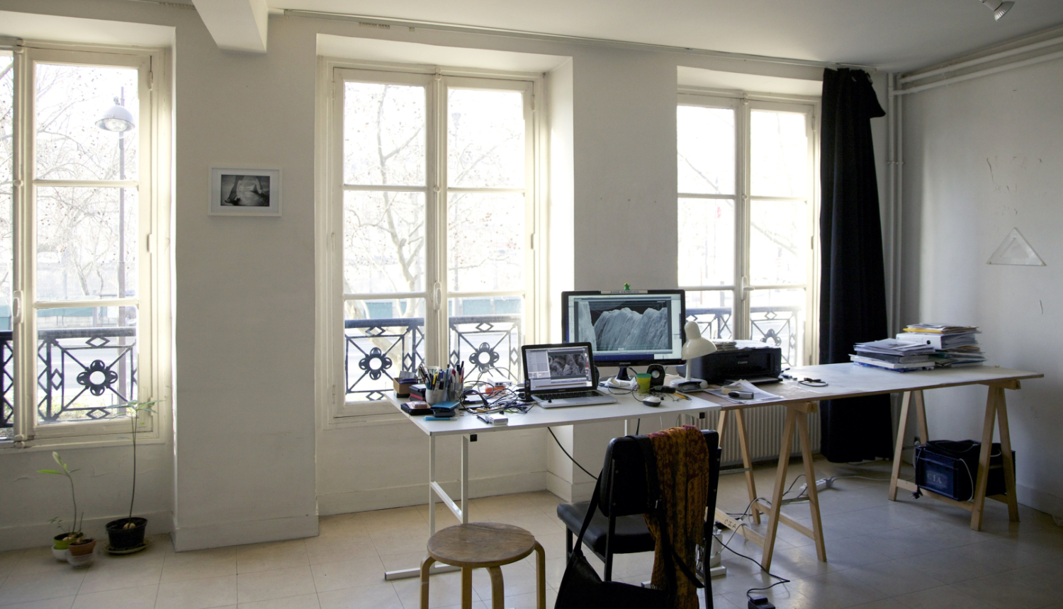 Cite Internationale des Arts gaiša darba vieta ar logiem. Uz galda datori, kancelejas piederumi