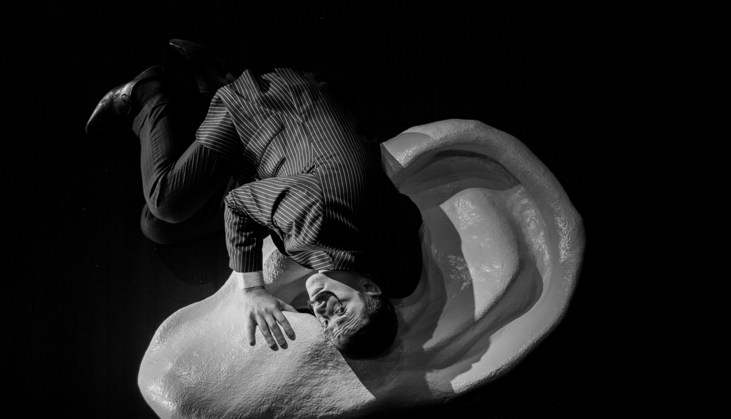 Melnbalts attēls - aktieris guļ uz lielas auss figūras