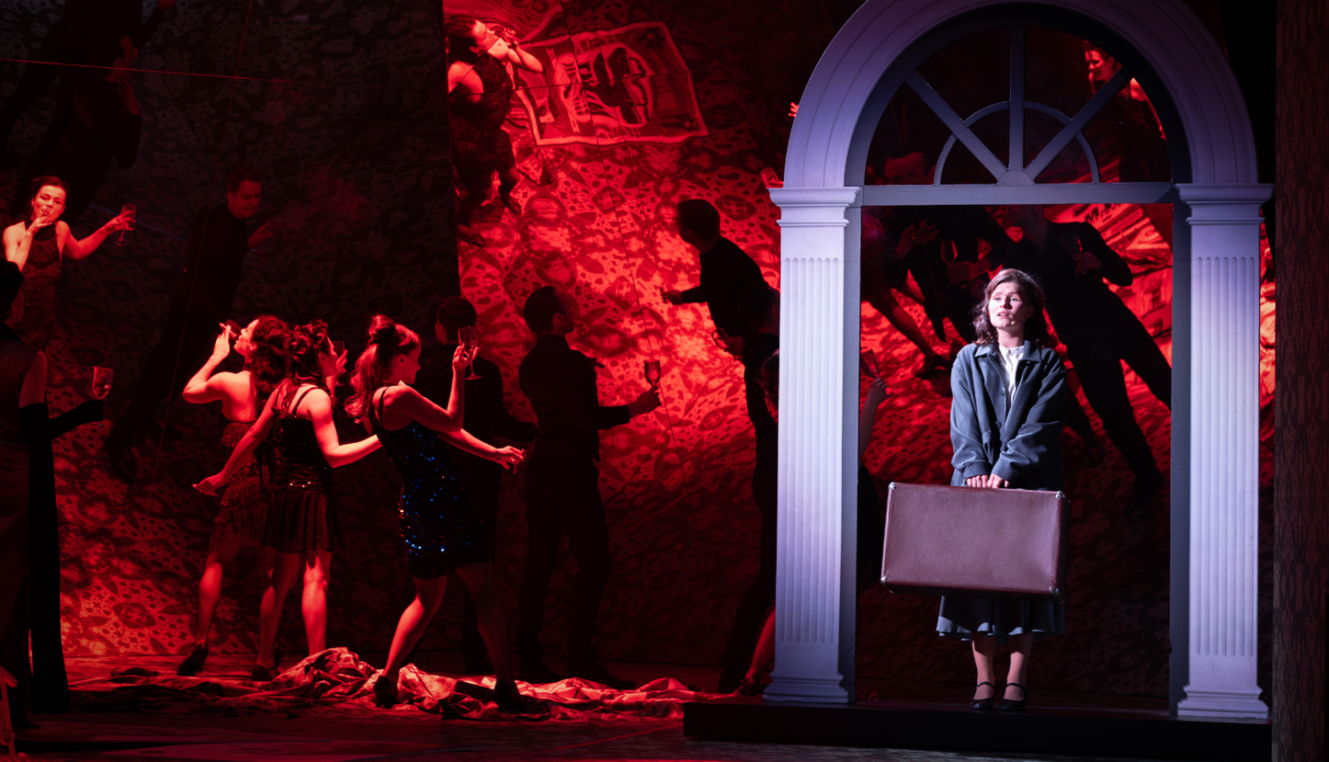 Skats no mūzikla - uz skatuves aktieri sarkanās gaismās