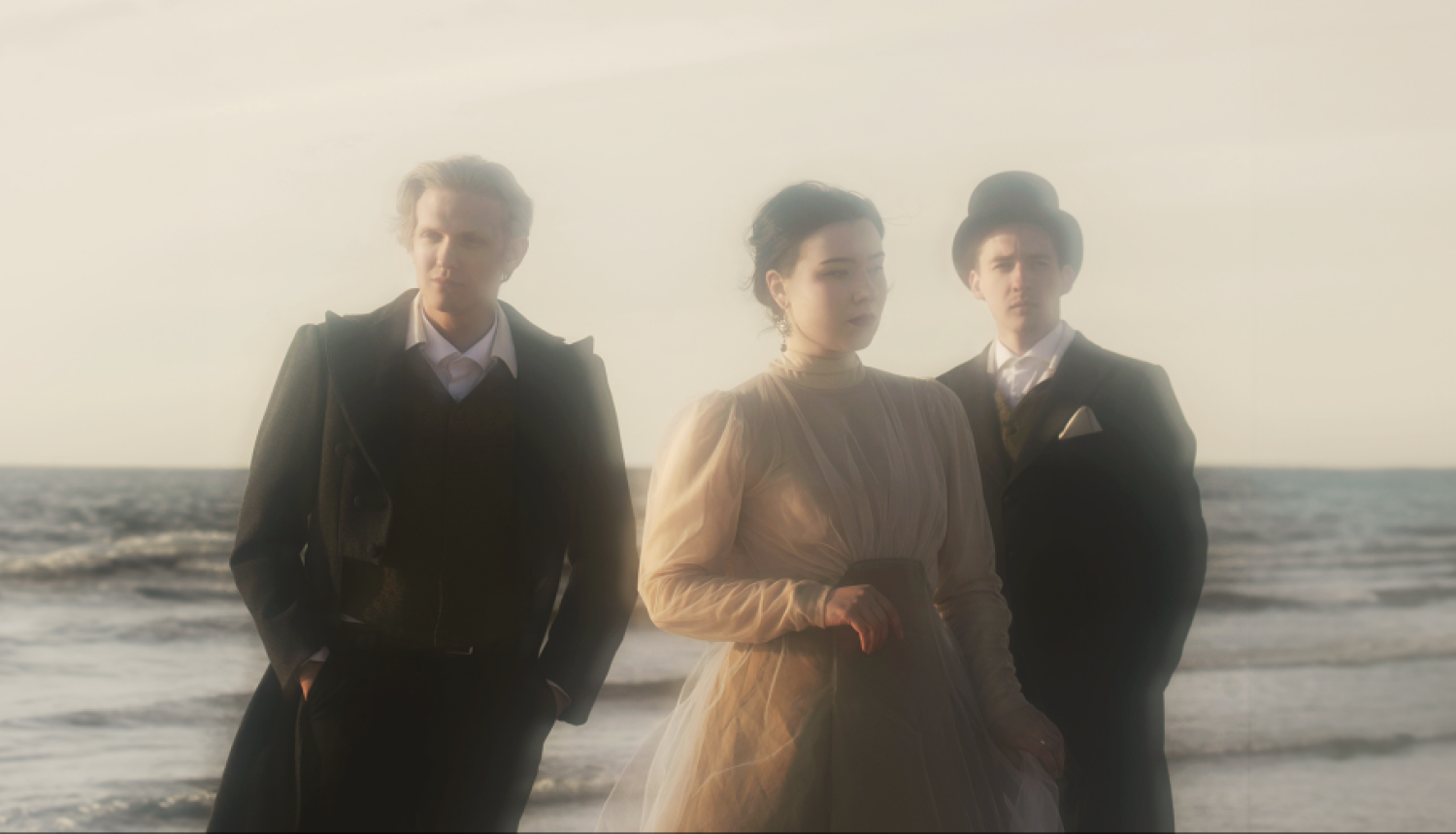 Trīs jaunie mākslinieki – soprāns Etīna Emīlija Saulīte, pianists Daniils Mickevičs un aktieris Artis Jančevskis uz jūras fona