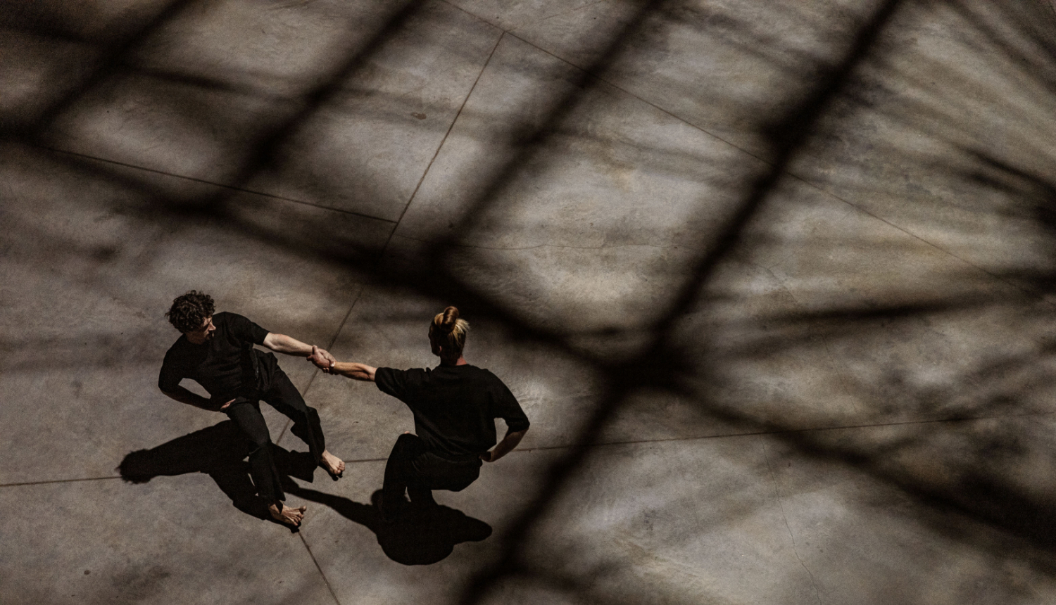 Divi cilvēki noēnotā telpā dejo tukša laukuma vidū