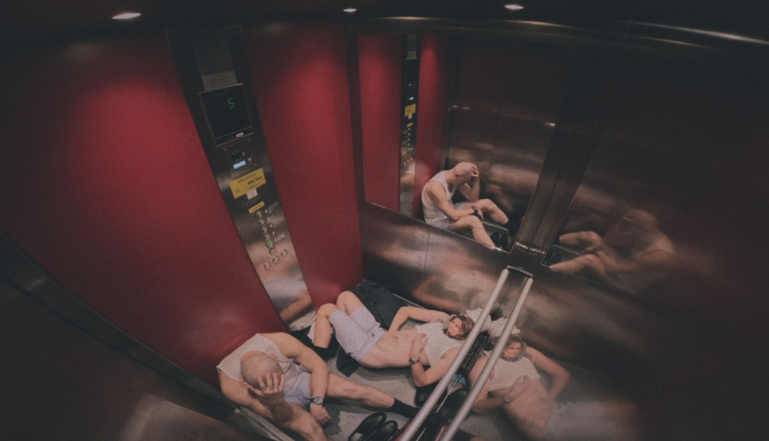 Stopkadrs no filmas “No No Place Hotel“, divi cilvēki liftā sēž uz grīdas