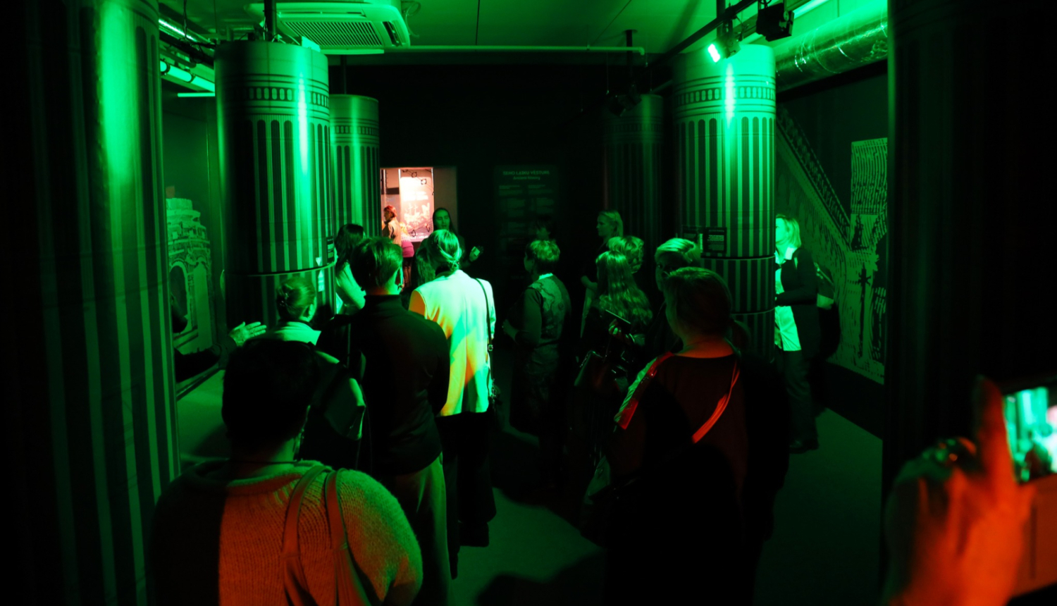 Cilvēki klausās izziņu centra zaļi apgaismotā telpā