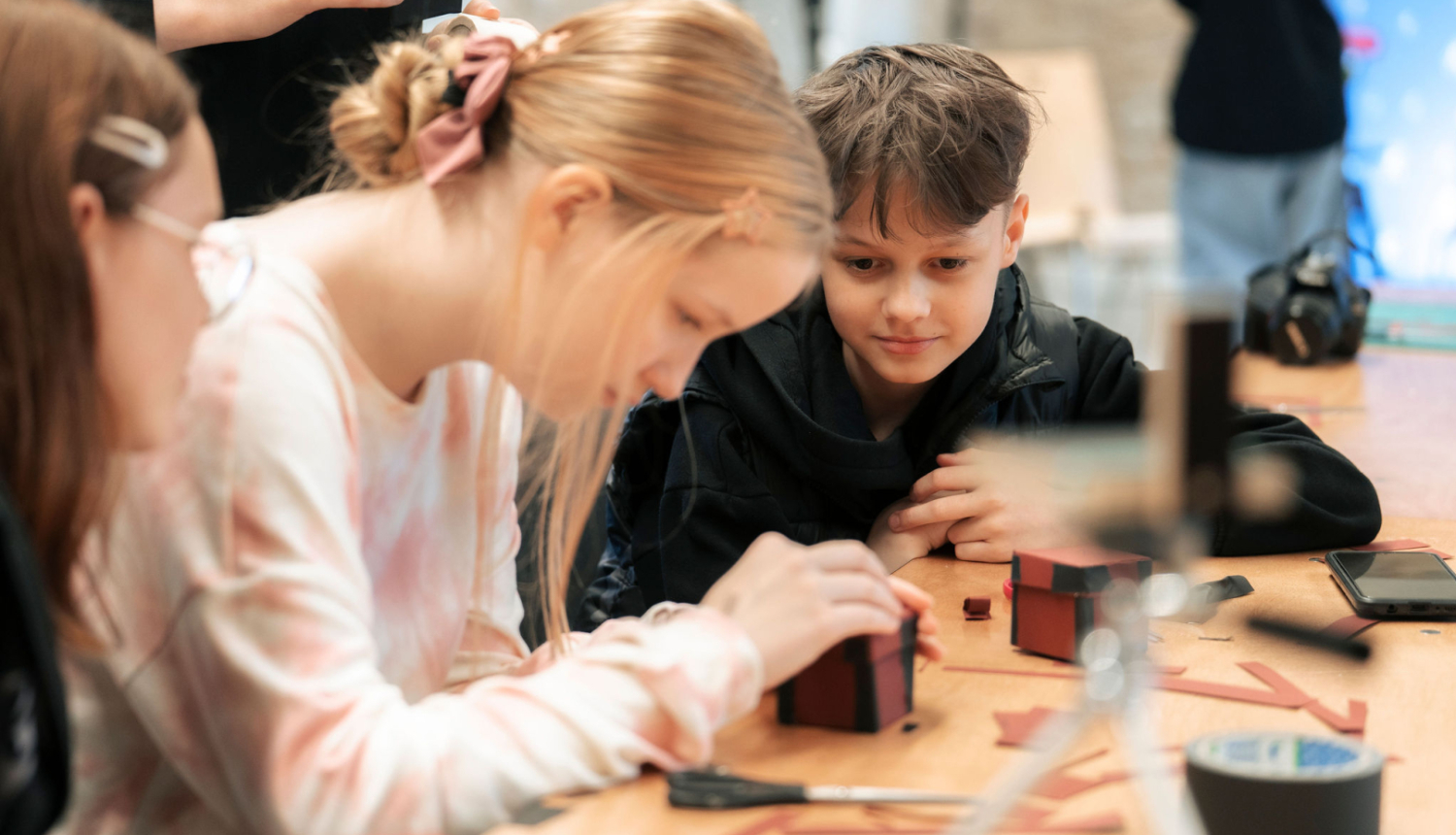 Bērni sēž pie galda, veido kastītes biedrības “ISSP” darbnīcā “Radošā fotogrāfijas laboratorija”