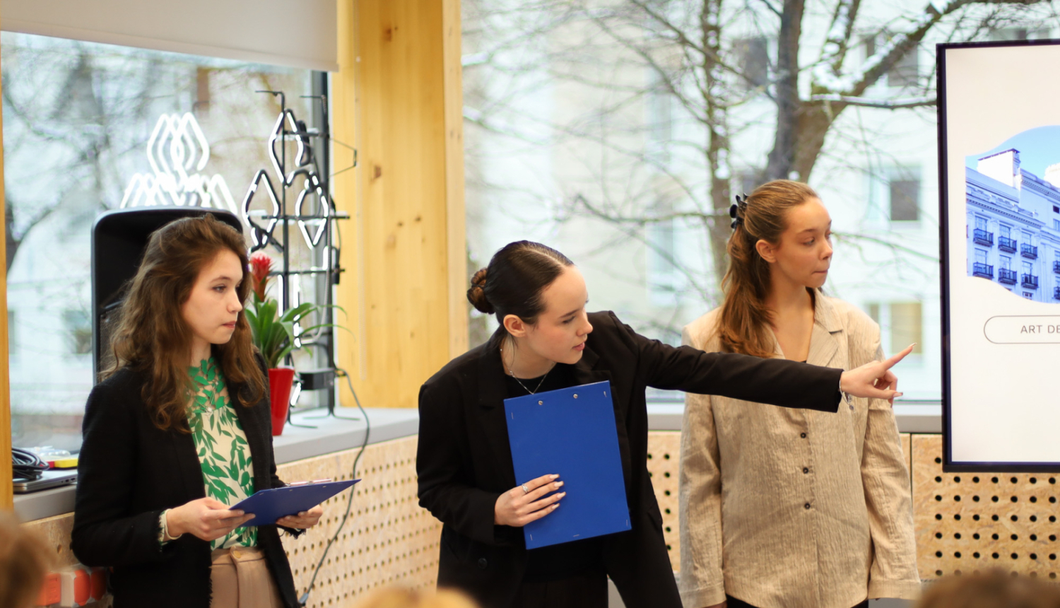 Trīs jaunietes prezentē projektu auditorijas priekšā