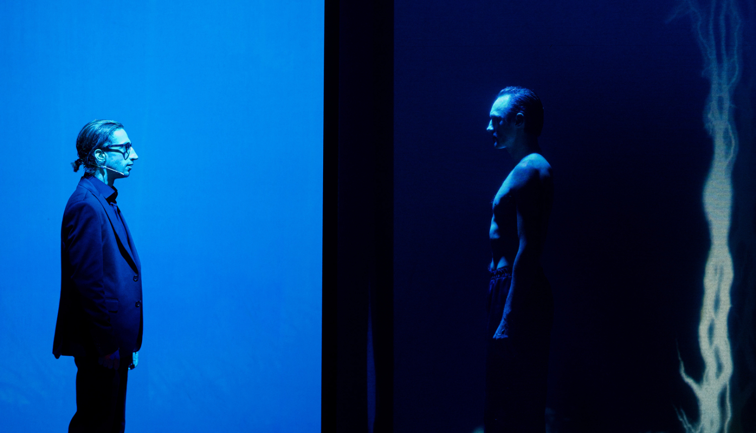 Daugavpils teātra izrādes “Kaids nūteikti atīs” (“Kāds noteikti atnāks”) aktieru silueti uz skatuves zilas krāsas apgaismojumā