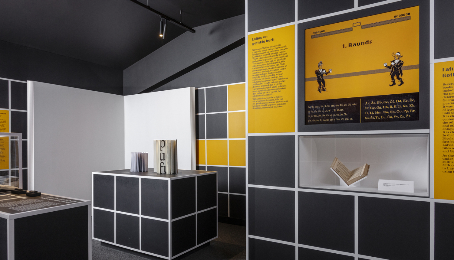 Latvijas Nacionālās bibliotēkas izstādes ekspozīcija, paneļi tumši pelēkā un dzeltenā krāsā, izstādes eksponāto