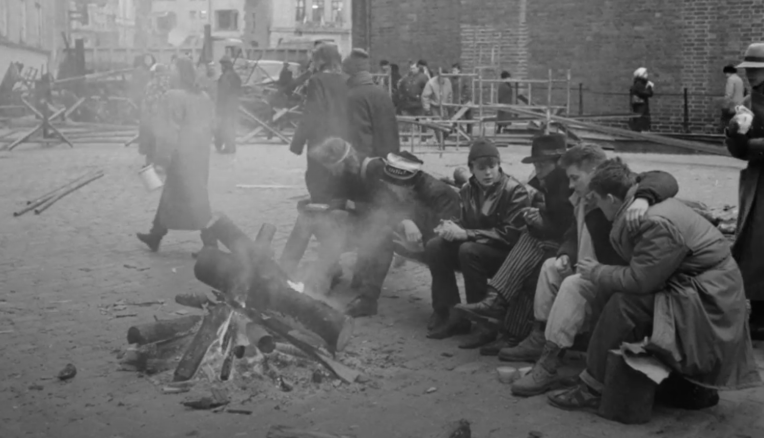 Kadrs no filmu materiāla. Cilvēki sēž pie ugunskura barikāžu laikā.
