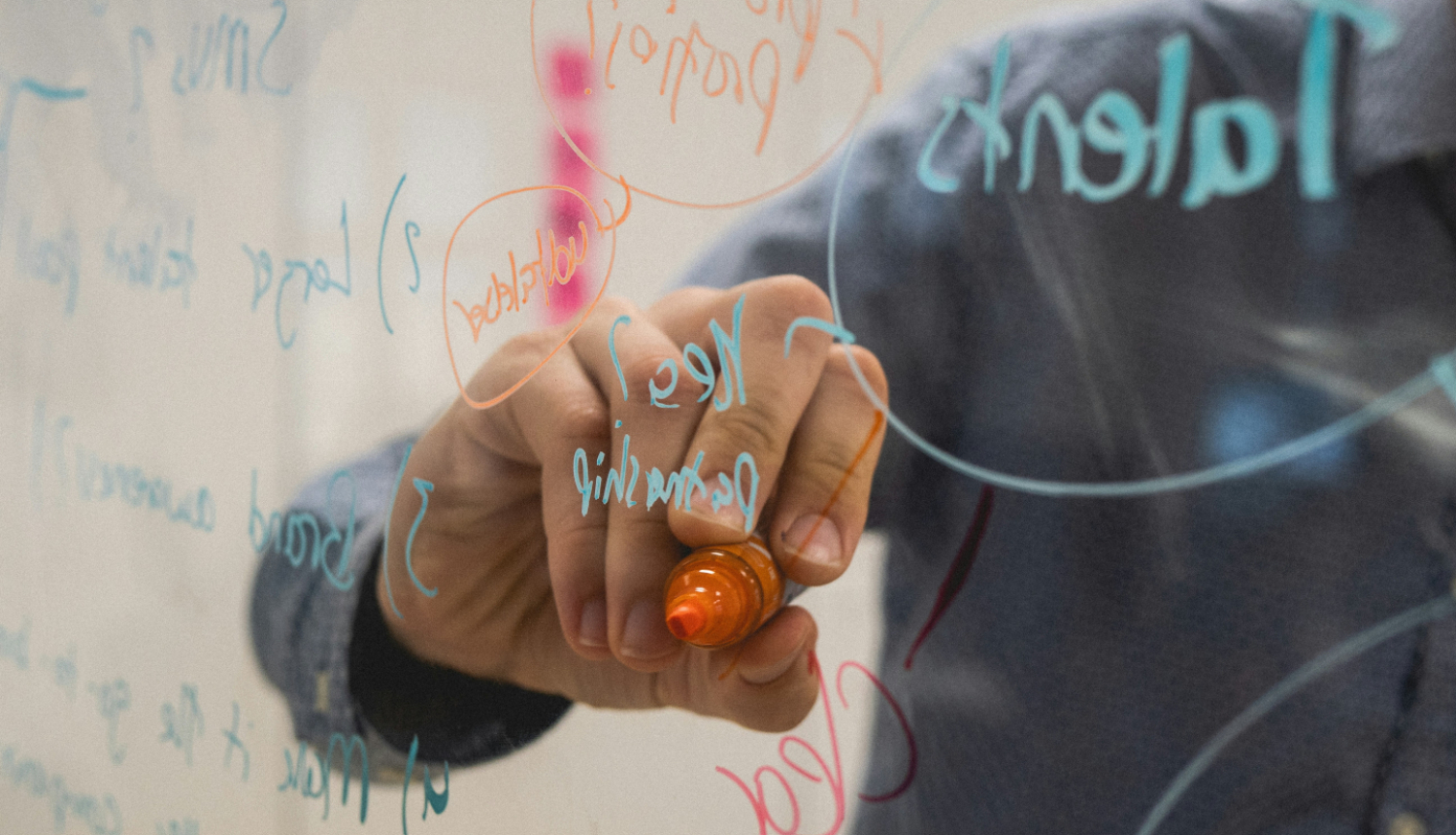 Cilvēks raksta ar marķieri uz caurspīdīgas/stikla tāfeles virsmas