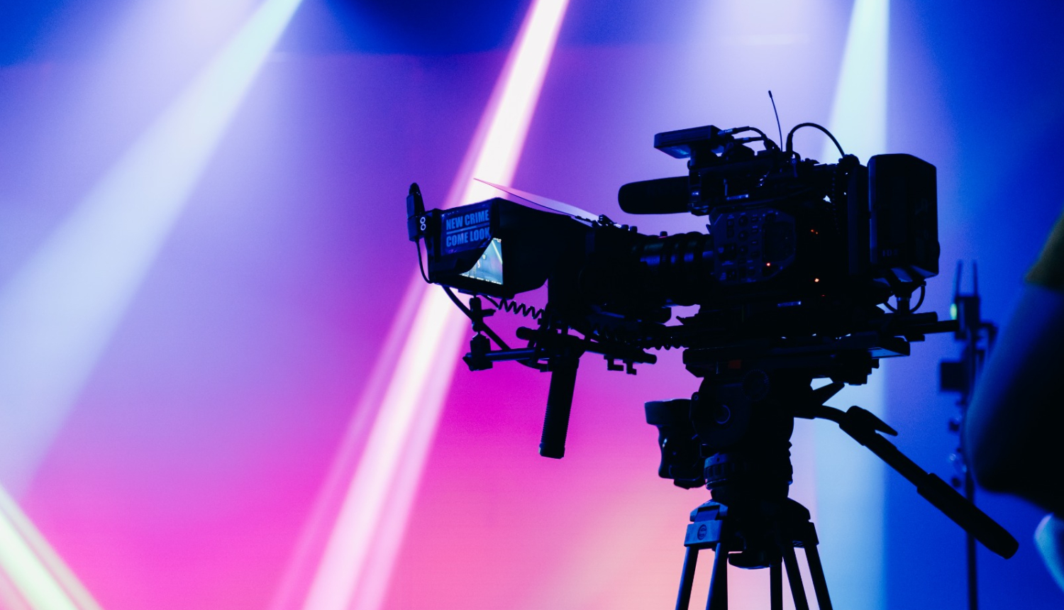 Latvijas Sabiedriskā medija publicitātes attēls. Filmēšanas kamera uz koši apgaismota fona.