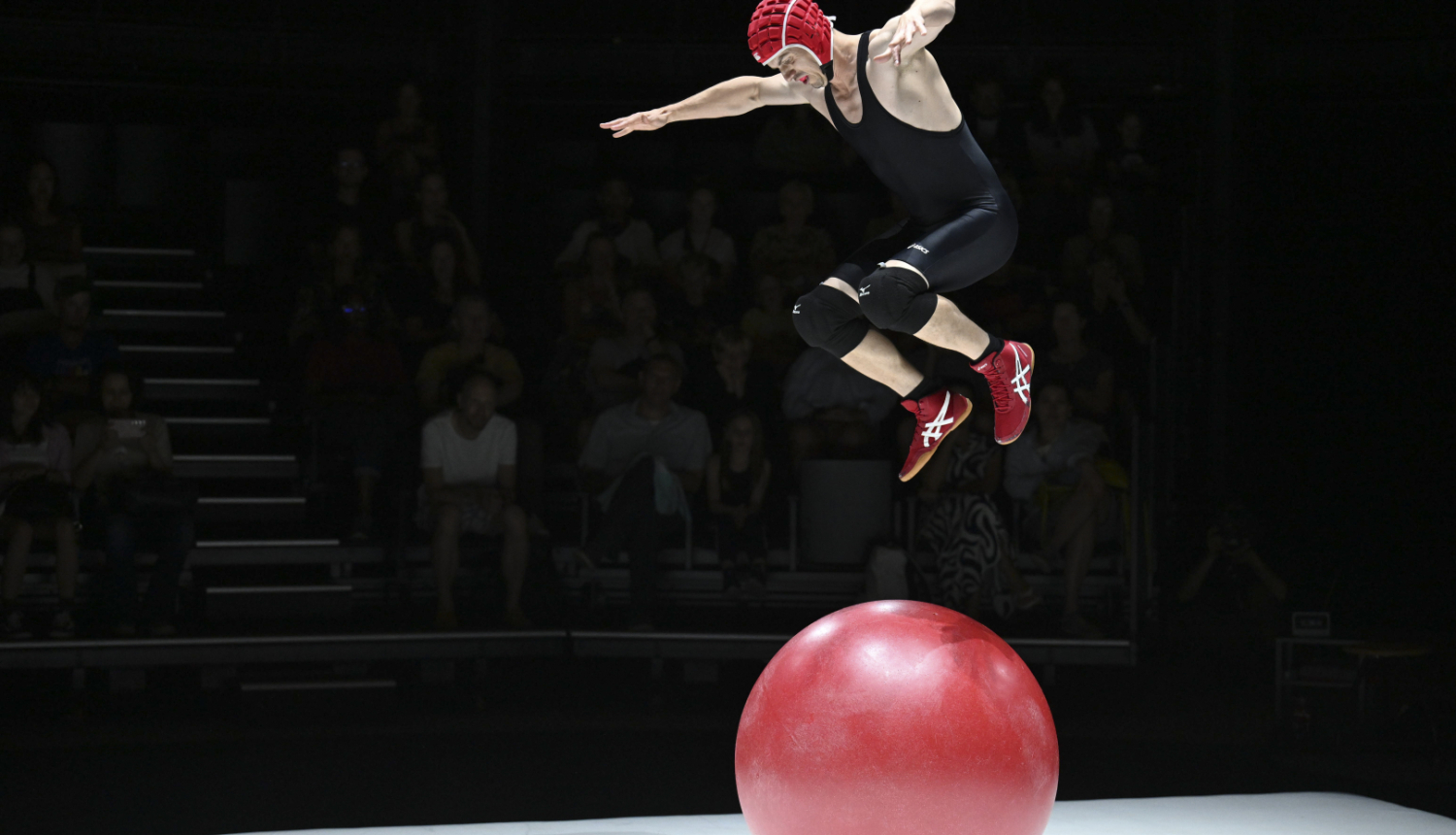 Cirka akrobāts arēnā izpilda vingrojumu uz sarkanas bumbas