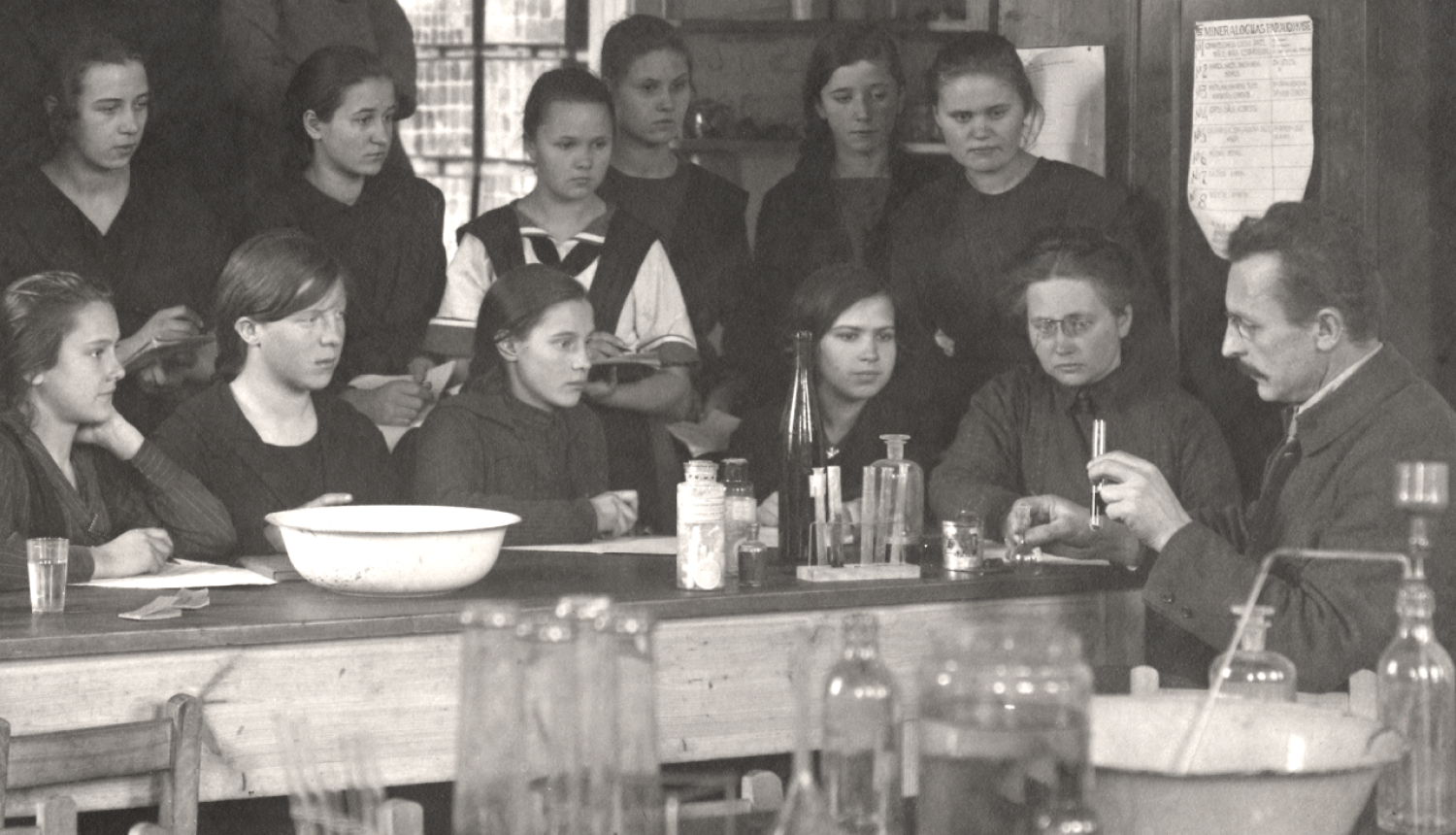 Semināra publicitātes attēls - sens melnbalts foto ar skolotāju un audzēkņiem mācību nodarbībā skolā