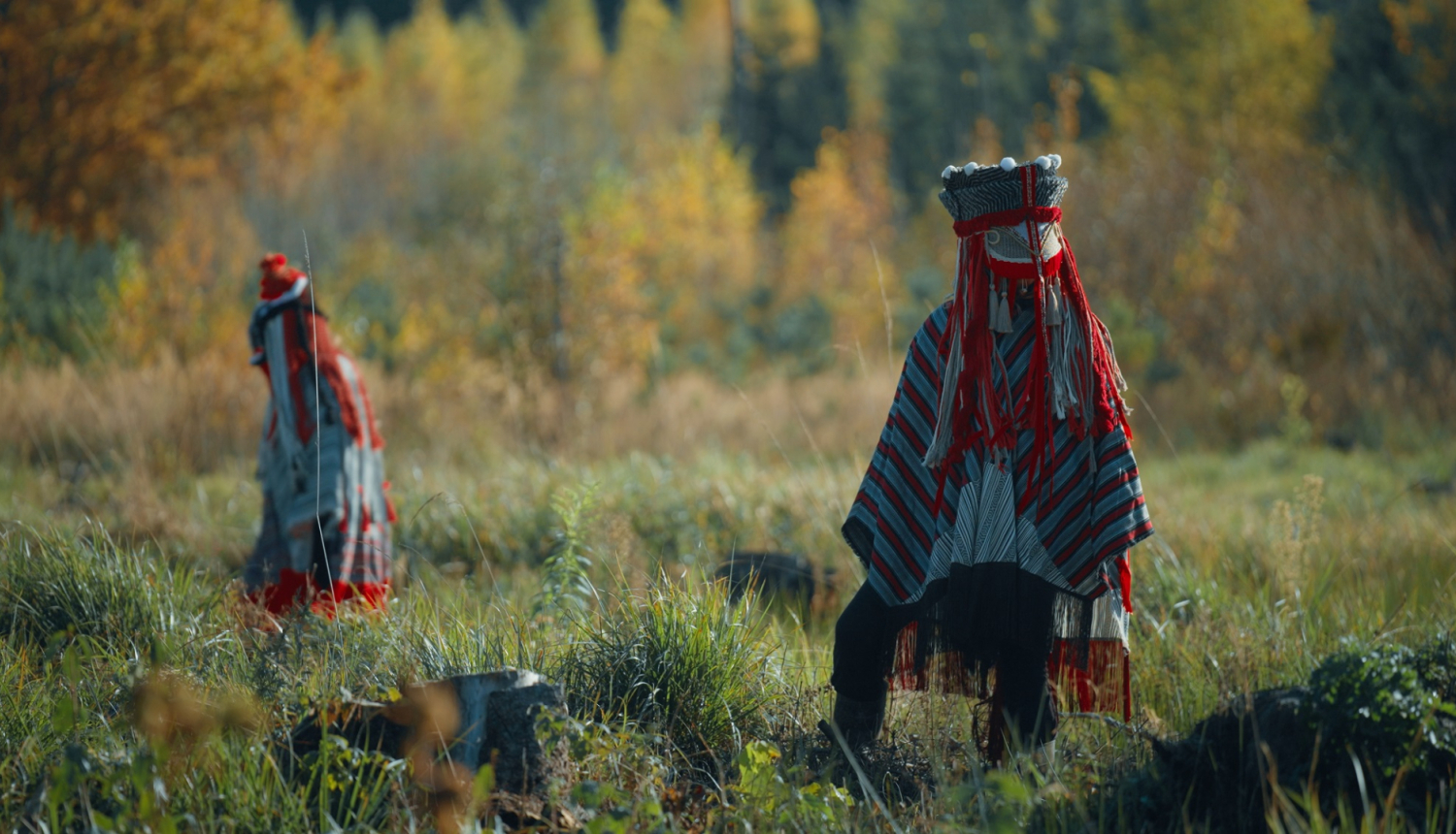 Kadrs no filmas - divi tēli etnokultūras stilistikas maskās rudenīgā mežmalas ainavā