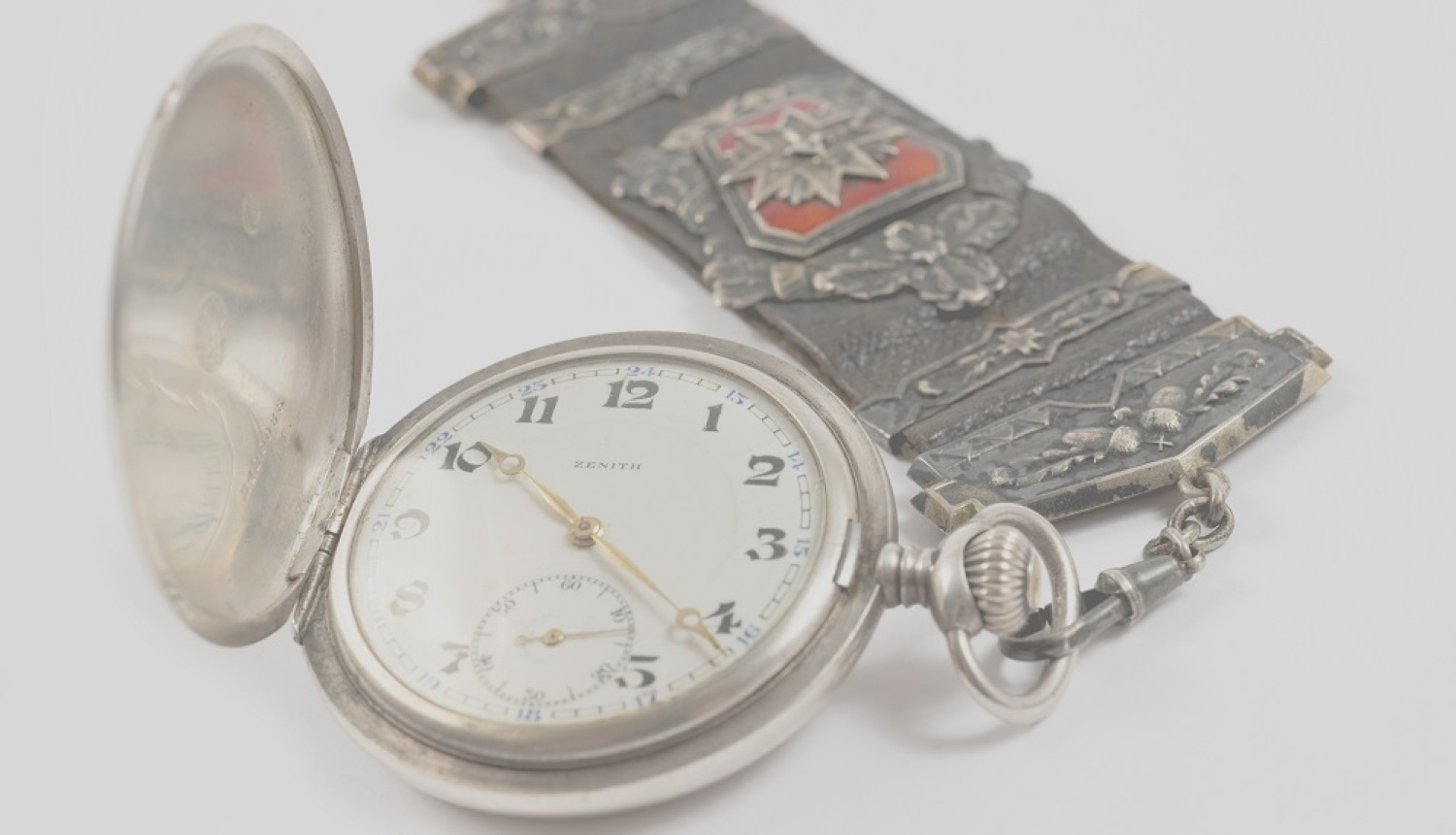 Pulksteņa breloks ar Latvijas Aizsargu organizācijas simboliku, piekārts pie kabatas pulksteņa “Zenith”.