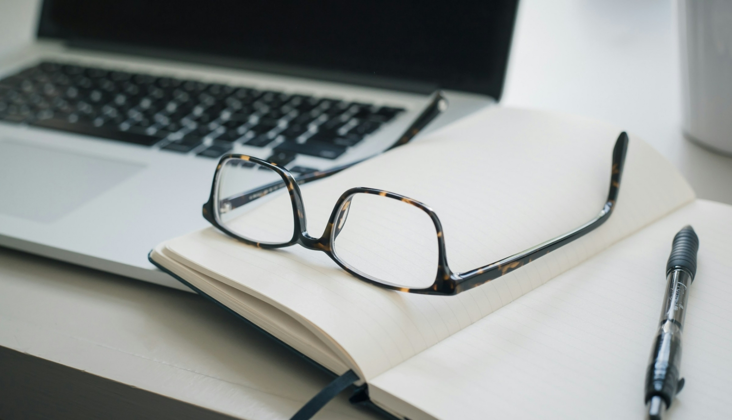 Dators, piezīmju blociņš un brilles uz galda