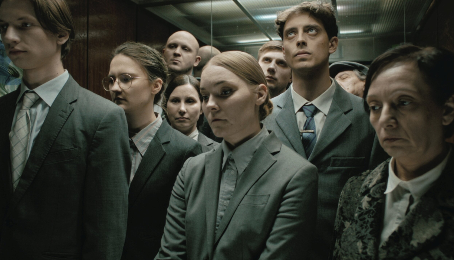 Kadrs no īsmetrāžas filmas “Kur saulīte nakti guļ?” - kadrā cilvēku grupa liftā