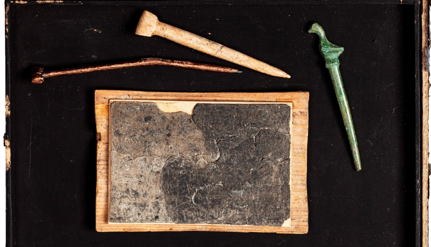 Izstādes “Viduslaiku Rīgas rakstāmlietas” publicitātes attēls. Kompozīcijā vaska tāfelīte un rakstāmirbuļi – stili.