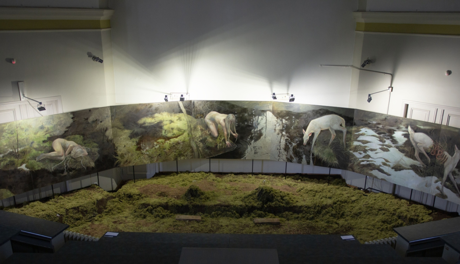 Apbalvotais darbs "Forest Floor" (2025) sūnas uz grīdas un sirreālas meža ainavas gleznotas uz vertikālām plaknēm apkārt sūnu laukam