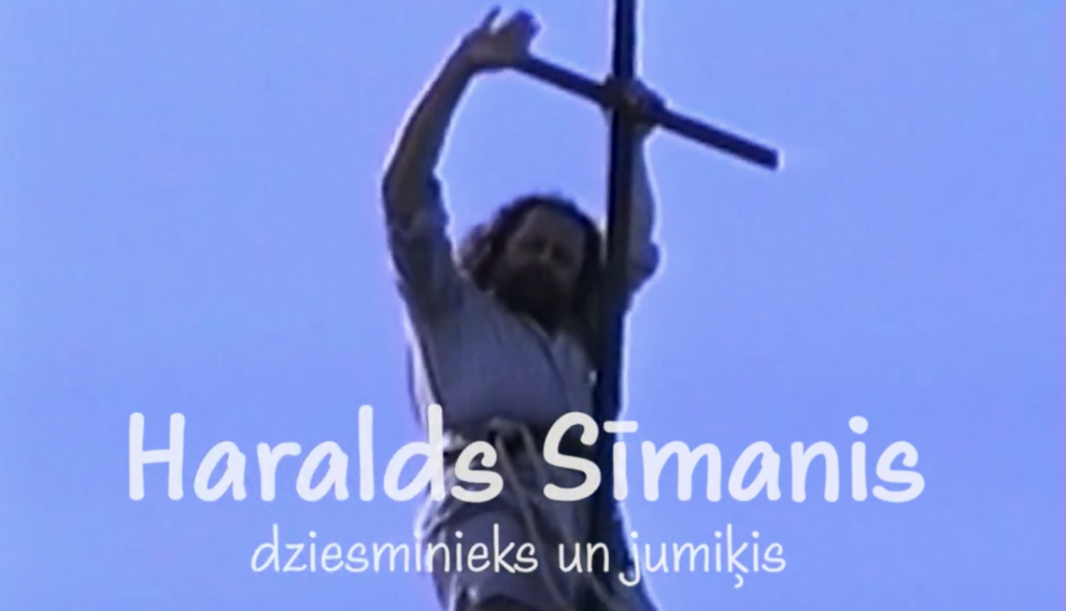 Filmas kadrs ar mūziķi Haraldu Sīmani un koka krustu. Teksts: Haralds Sīmanis, dziesminieks un jumiķis