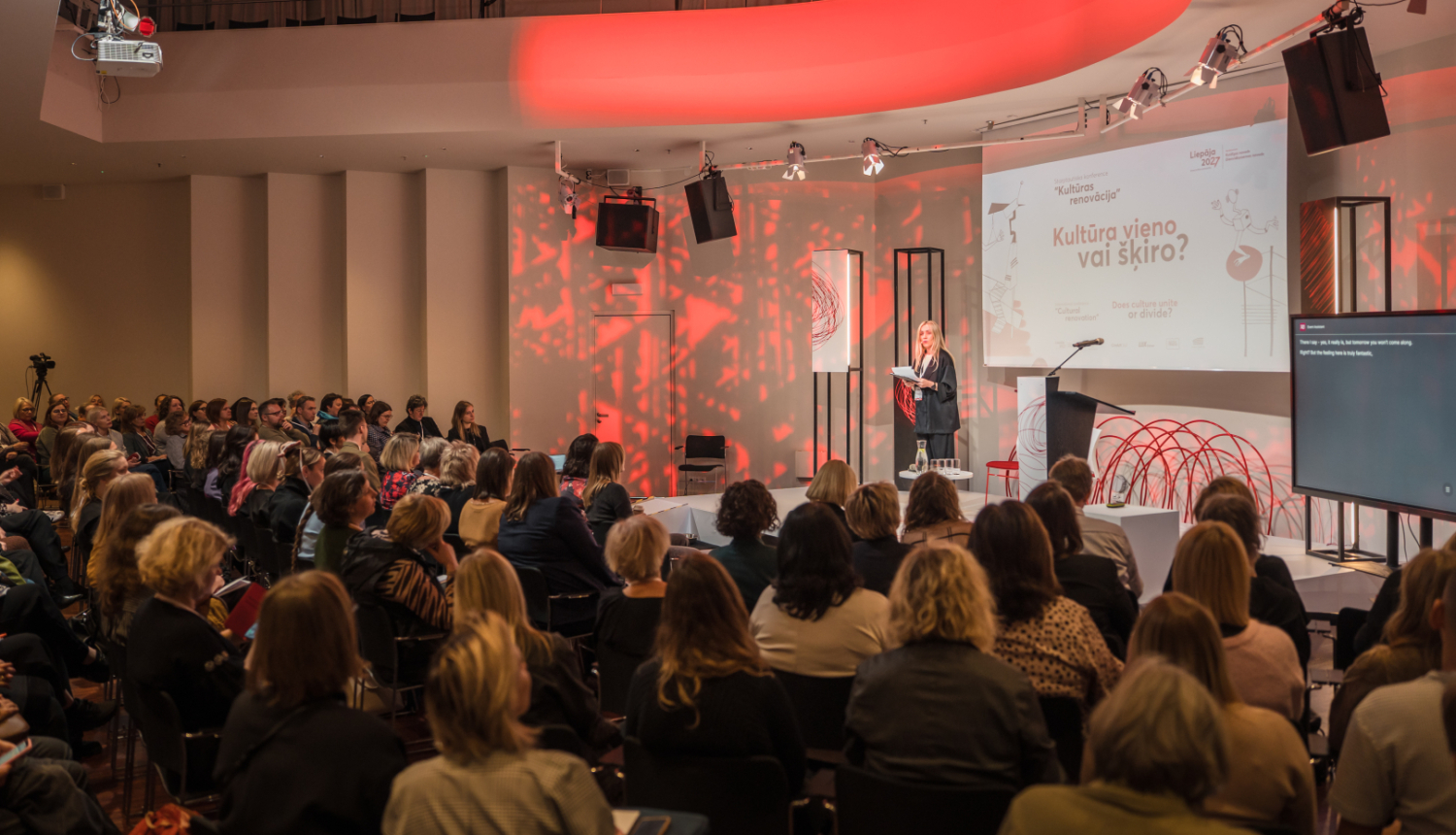 "Liepāja - Eiropas kultūras galvaspilsēta 2027" konferences norise ar pasākuma moderatoru uz skatuves un skatītājiem zālē