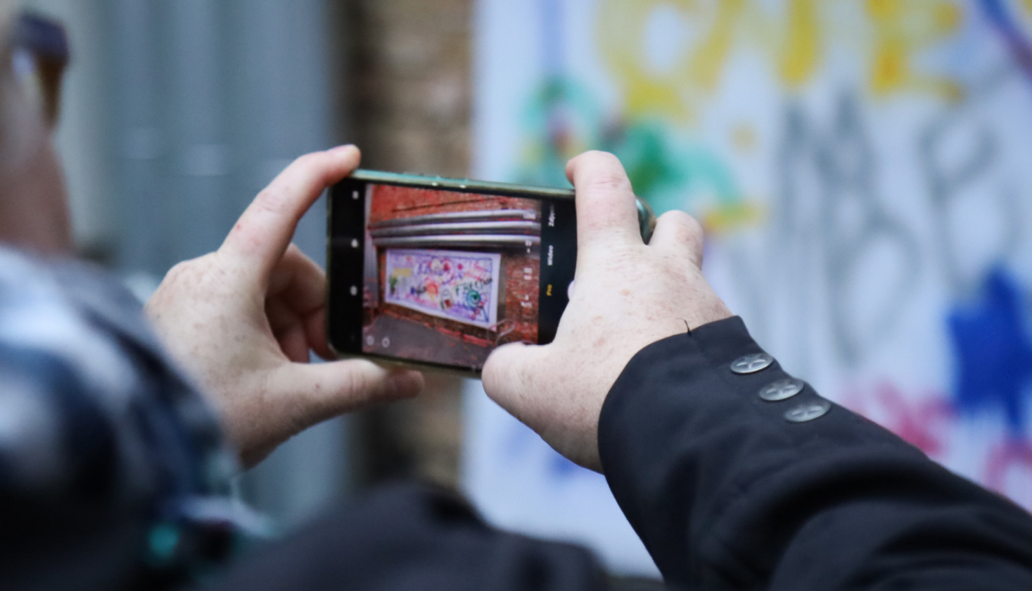 Rokas ar telefonā atvērtu kameras aplikāciju